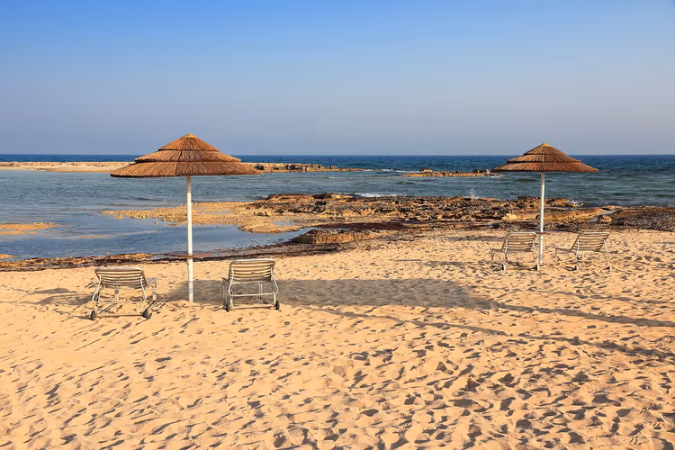 Sandstrand von Ayia Thekla mit Sonnenschirmen und Liegen