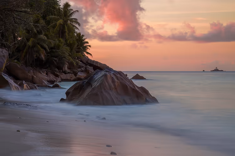 Granittblokker og palmer på La Digue-stranden ved solnedgang
