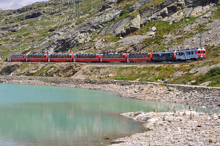 roter Bernina-Express-Zug an einem See in den Alpen
