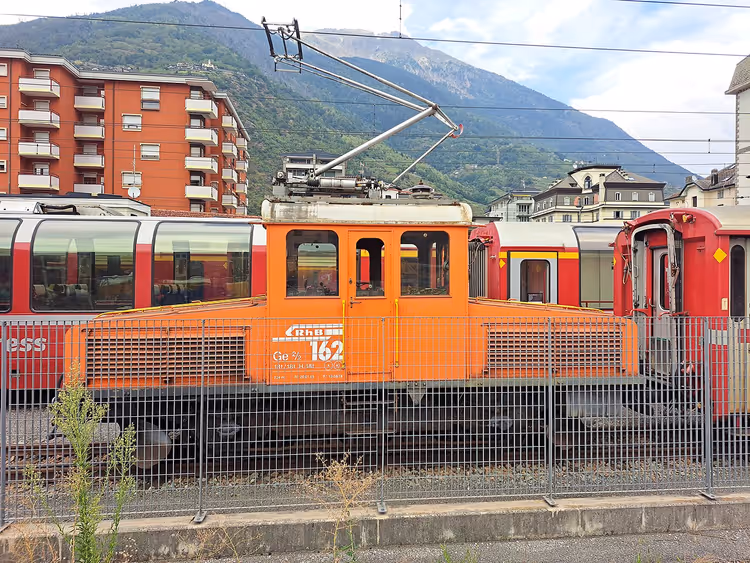 Orange Lokomotive und rote Züge im Bahnhof Tirano