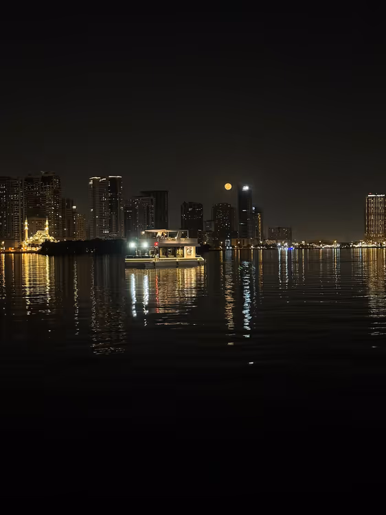 Ночная набережная Шарджи с огнями и катером на воде
