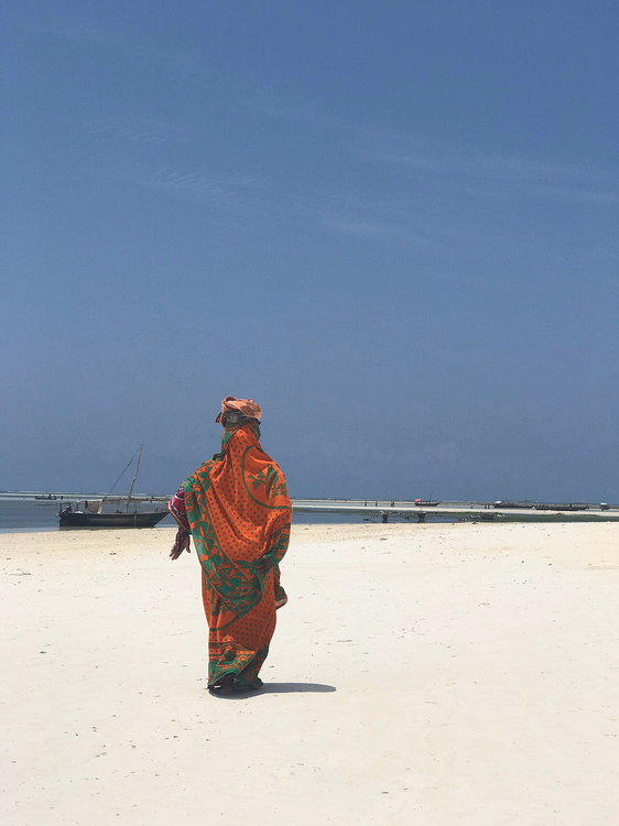 Vrouw in een kanga op het witte zandstrand van Nungwi