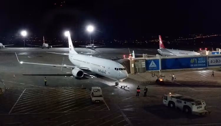 Plataforma do Aeroporto de Tbilisi à noite com uma aeronave no portão
