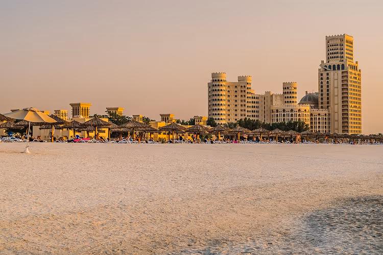 Al Hamra Beach med parasoller og hoteller i solnedgang