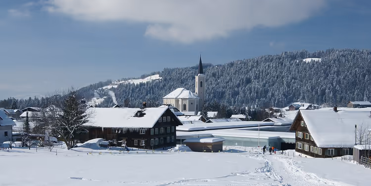 Snødekt landsby Alberschwende med kirke og hus om vinteren