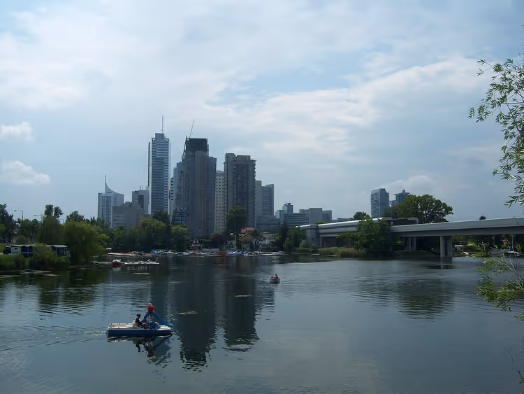 Pratiquants de stand-up paddle sur l'Alte Donau avec des gratte-ciel en arrière-plan