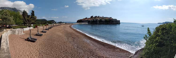Strand med solsenger og øya Sveti Stefan