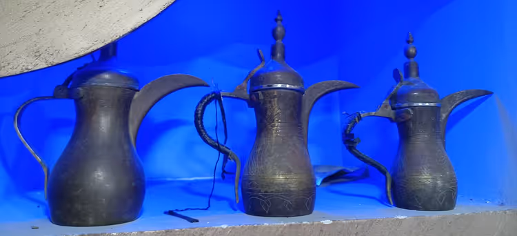 Tre arabiske dallah-kaffekanner på en blå hylle