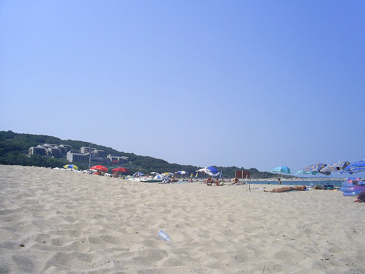 Zandstrand met parasols bij beboste heuvels