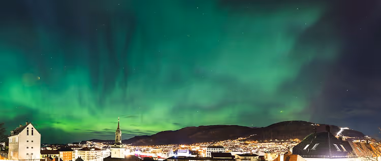 Groen noorderlicht boven een stad en bergen in de nacht