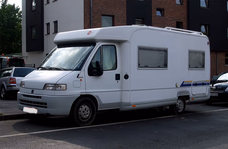 Hvit delintegrert Bürstner-bobil ved siden av en bygning