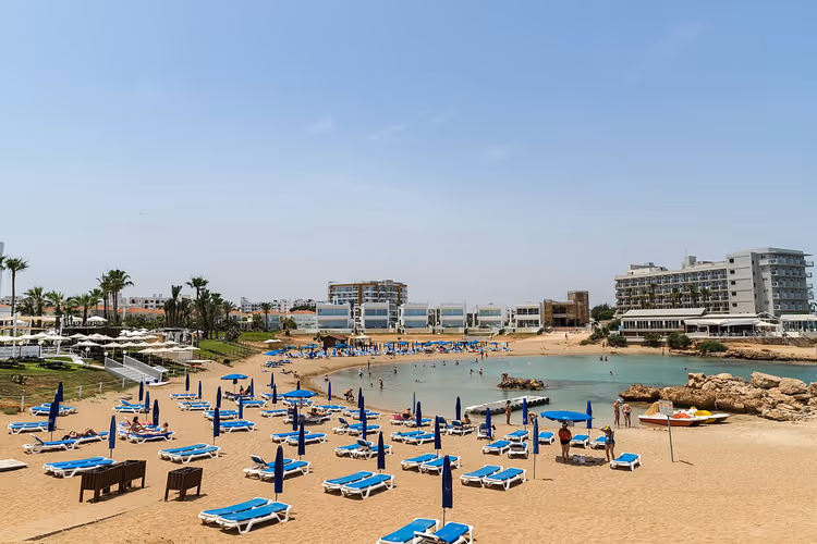 Arka planda mavi şezlonglar ve otellerle plaj