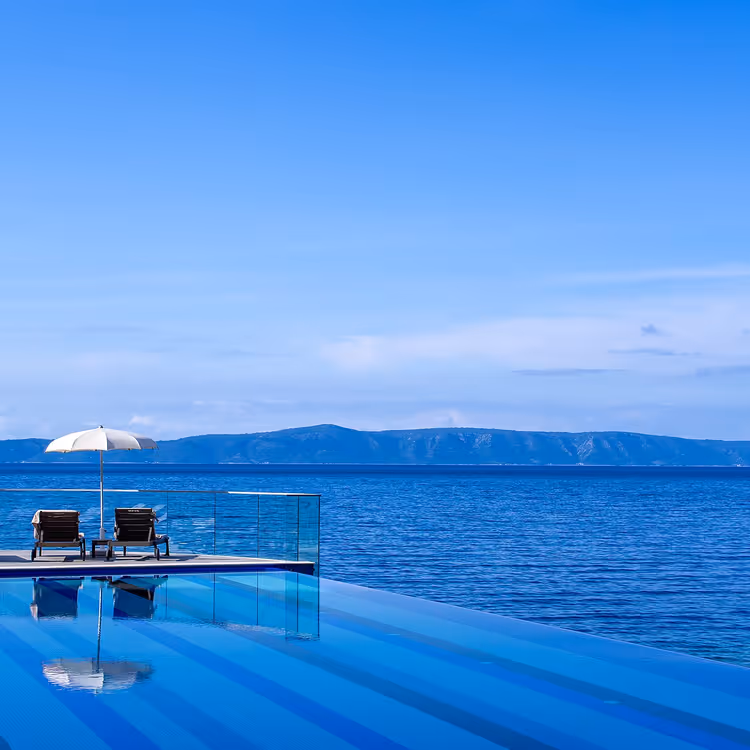 Infinitypool met ligstoelen en uitzicht op zee en bergen