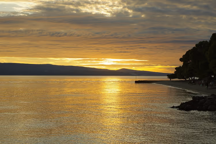 Zonsondergang boven zee met bergen en bomen langs de kust