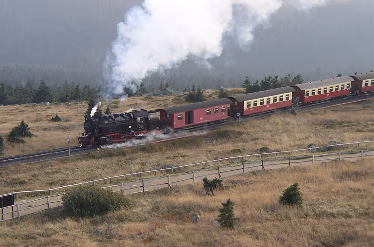 Stoomlocomotief van de Brockenbahn met rijtuigen tegen een bergachtergrond