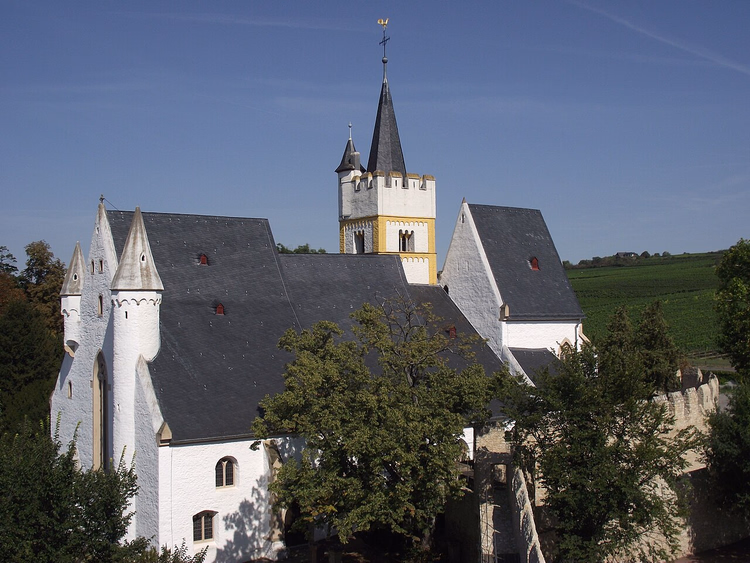 Weiße Burgkirche von Ingelheim zwischen Bäumen und Weinbergen