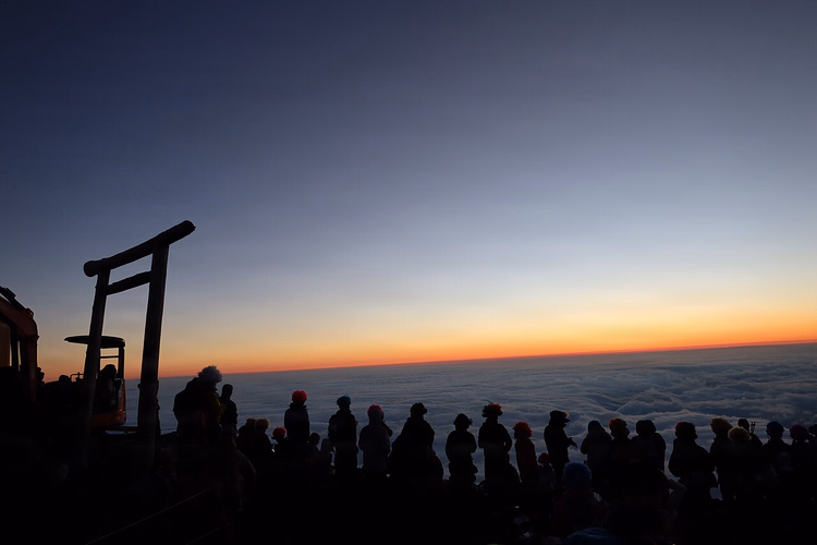 Fuji Dağı'nın zirvesindeki torii kapısında gün doğumunu izleyen tırmanıcılar