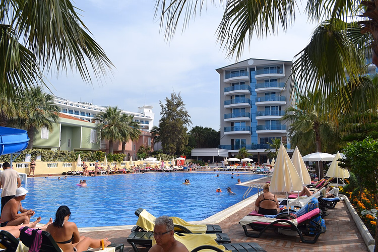 Palmiyeler arasındaki otel binasının yanında şezlonglu havuz