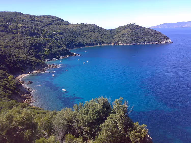 la baia di Cala Grande con acqua turchese e colline boscose