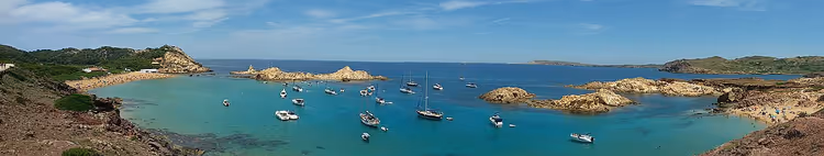 Panorama van Cala Pregonda-baai met boten en kliffen