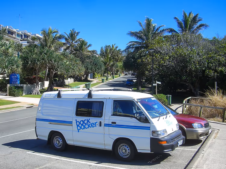Hvit camper med backpacker-bokstaver blant palmer
