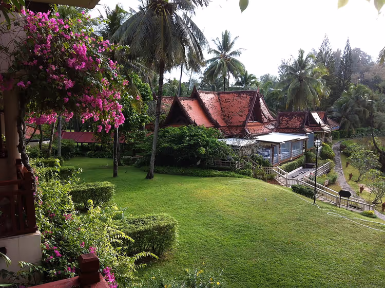 Thailandske tak på resortbygg blant palmer og plen