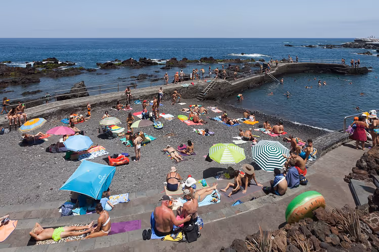 Folk som slapper av på en strand med mørk sand og steiner