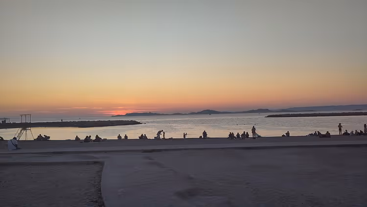 Solnedgang ved Prado-stranden med silhuetter av badende