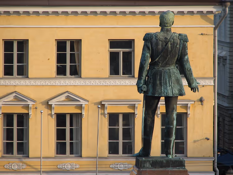 Bronsemonument over Alexander II bakfra ved en gul bygning