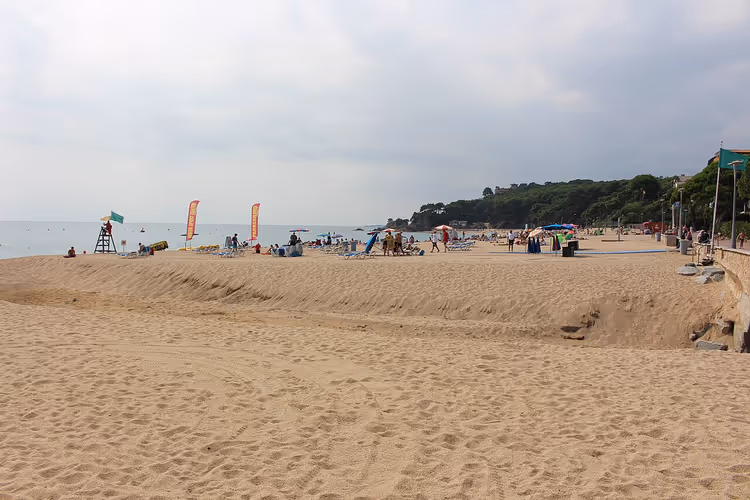 Sandstrand med havet, mennesker og en grønn ås