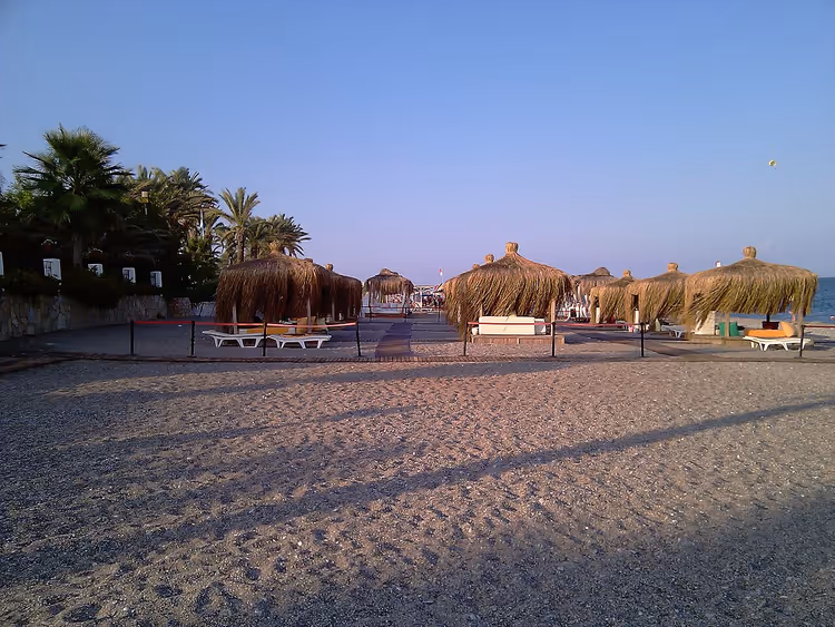 Rullesteinstrand med stråparasoller og solsenger