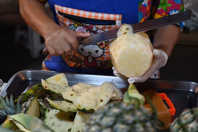 Straatverkoopster snijdt een rijpe ananas in plakken met een mes