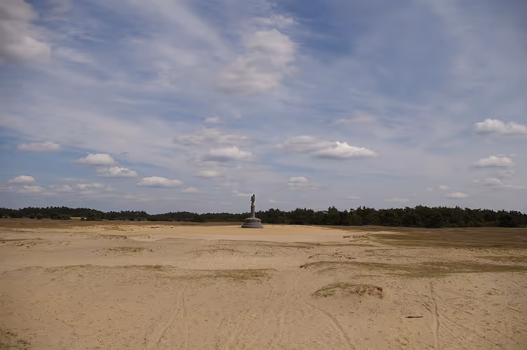 Sandige Ebene mit einer Statue und Wald in der Ferne