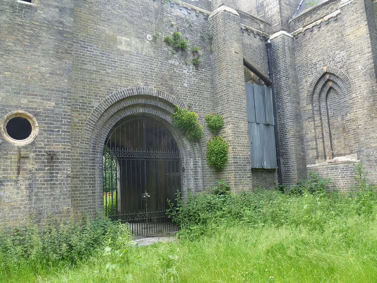 Oude bakstenen kapel met traliehek in verwilderd groen