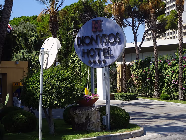 Dionysos-hotelsign tussen palmbomen en groen