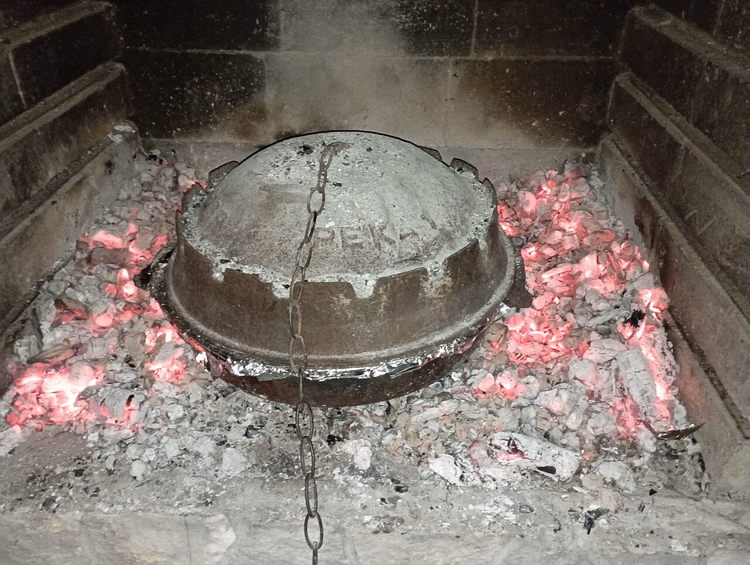 Pekaglocke über glühender Holzkohle in einer Feuerstelle