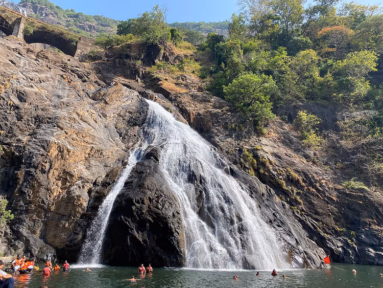 Dudhsagar-Wasserfall am Felsen, unten badende Menschen