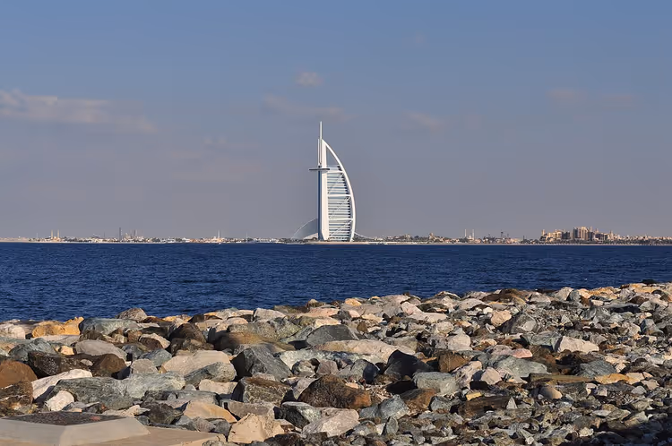 Burj Al Arab i det fjerne bortenfor havet, steinete strand