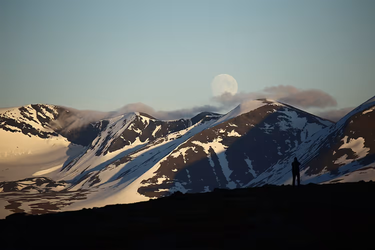 Vollmond über den schneebedeckten Bergen von Abisko und die Silhouette eines Fotografen