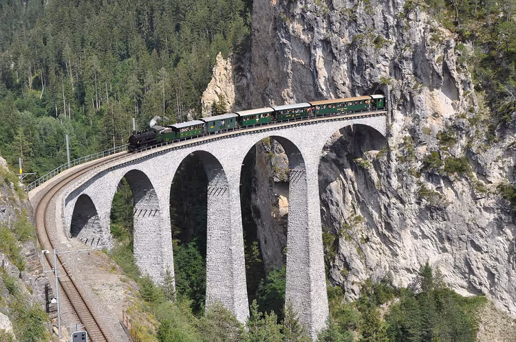 Geschwungenes Steinviadukt mit einem Zug zwischen Felsen