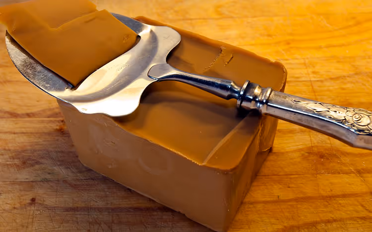 Gümüş peynir dilimleyiciyle kahverengi brunost peyniri bloğu