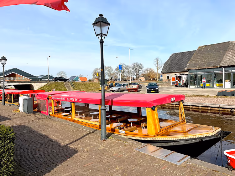 Turistbåt med rødt tak ved en brygge i Giethoorn