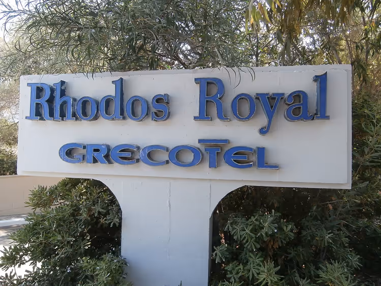 Blått skilt for Rhodos Royal Grecotel hotell blant busker