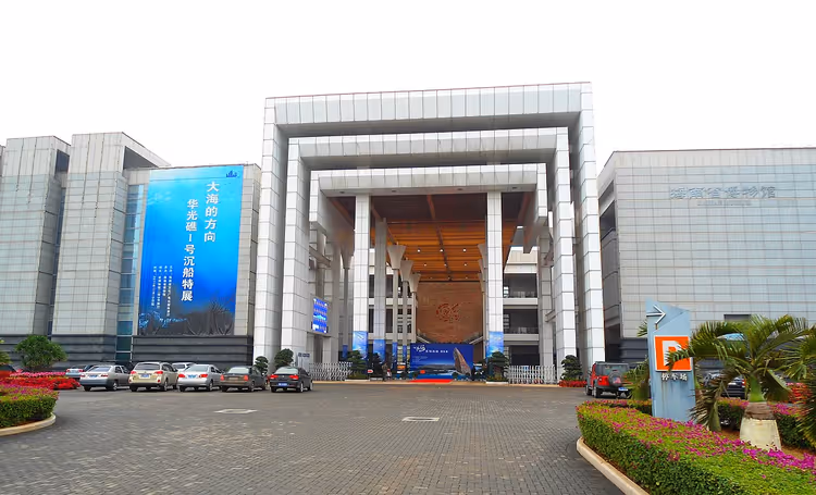 Gevel van het Hainan Museum met een tentoonstellingsbanier en parkeerplaats