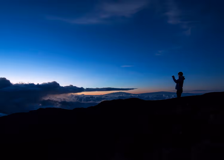 Silhouette eines Wanderers am Kraterrand über den Wolken bei Sonnenaufgang