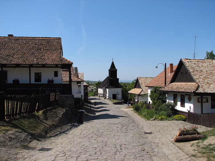 Kopfsteinpflasterstraße in Hollókő mit weiß getünchten Häusern und einer Kirche