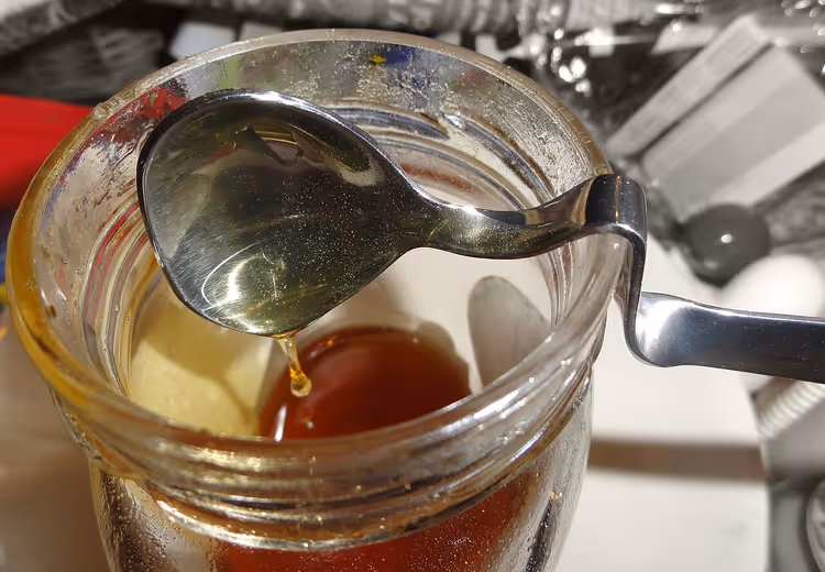 عسل يقطر من ملعقة في برطمان زجاجي في المطبخ