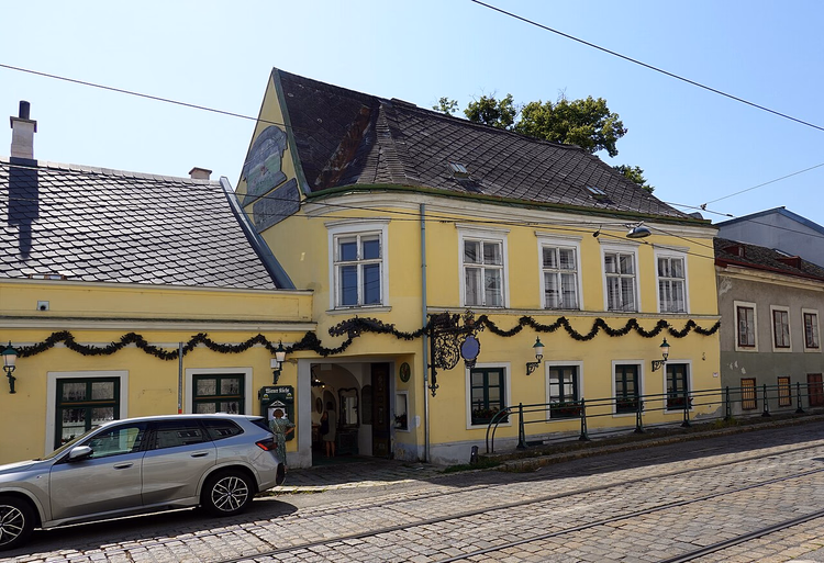 Gelbe Fassade eines Heurigen an den Straßenbahngleisen