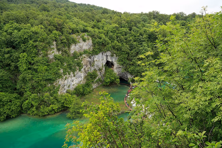 Parete rocciosa con l'ingresso alla Grotta Šupljara sopra un lago turchese