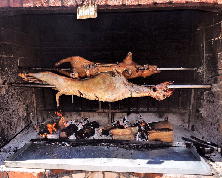 Lamb and suckling pig on spits over coals